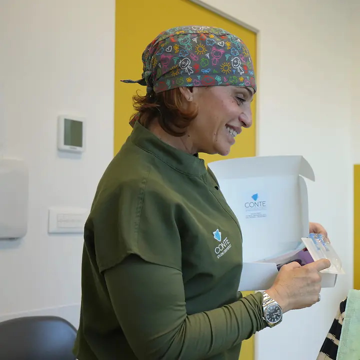 La Dott.ssa Antonella Conte sorride aprendo una scatola di mascherine trasparenti, davanti a una parete gialla