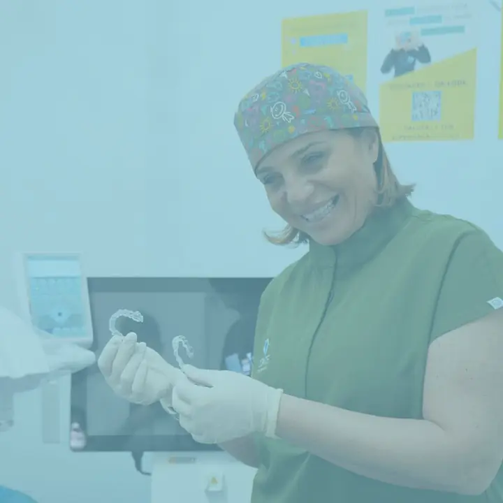 La Dott.ssa Antonella Conte sorride guardando una mascherina trasparente, accanto allo schermo con una radiografia
